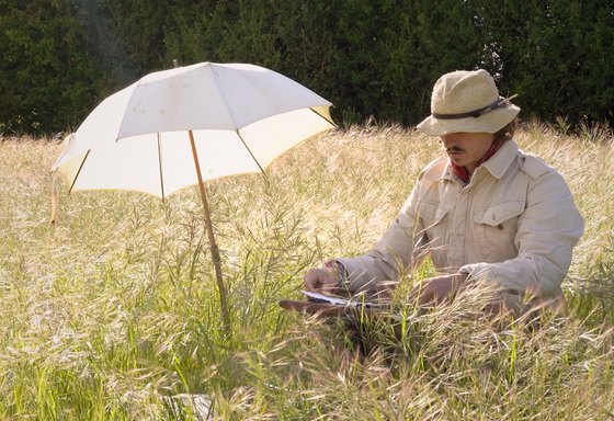 Carl-Johann de Nassau painting in a field of tall grass under a white umbrella